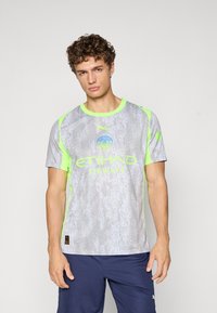 Szürke sportpóló texturált felülettel, amely cseppeket idéz, neon zöld ujjakkal és szegéllyel, logóval és szöveggel díszítve.