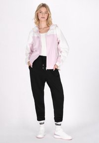 Lett pink og hvid jakke med hætte, lynlås lukning, elastiske manchetter; stylet med sorte joggere og hvide sneakers med pink accenter.
