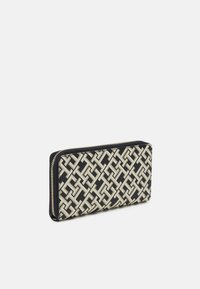 Portafoglio con zip caratterizzato da un motivo intrecciato in nero e crema. Il materiale sembra pelle con una texture liscia e bordi netti.