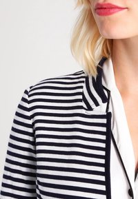 Blazer rayé en mélange de coton marine et blanc, présentant une coupe ajustée avec un col cranté et des boutons à l'avant.