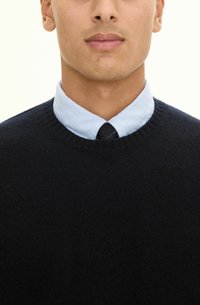 Granatowy sweter z okrągłym dekoltem noszony na jasnoniebieskiej koszuli z kołnierzykiem. Materiał wydaje się miękki o gładkiej fakturze, z prążkowanymi mankietami.