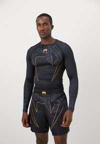 Haut noir de sport à manches longues et shorts avec motif de serpent jaune et accents, fabriqué en matériau extensible, design ajusté et texture lisse.
