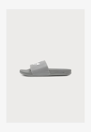 Μονό γκρι σανδάλι Adidas slide με λευκό λογότυπο στο λουράκι, υφασμένη πάτημα και φλατ σόλα σε απλό φόντο.