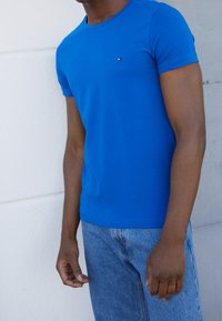 T-shirt en coton bleu à manches courtes, col rond et petit logo sur la poitrine. Porté avec un jean en denim bleu clair.