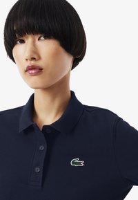 Navy-Polohemd aus strukturiertem Material mit einer Drei-Knopf-Leiste und einem kleinen gestickten Krokodil-Logo auf der Brust.