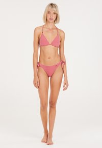 Różowy, teksturowany bikini z trójkątnym stanikiem z falbankami i regulowanymi ramiączkami; dopasowane majtki o niskim stanie z wiązaniami po bokach.