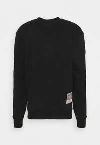 Sweat-shirt noir en coton doux, avec un col rond côtelé, des manches longues et une étiquette en bas à gauche.