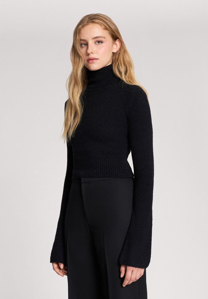 Czarny pulower z wysokim kołnierzem o teksturowanym wykończeniu oraz długimi, rozszerzającymi się rękawami, z dopasowaną talią i miękkim, elastycznym materiałem.