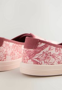 Zapatillas slip-on de lona con estampado floral en rosa claro y detalles en burdeos. Presentan un patrón floral texturizado y una suela de goma suave.