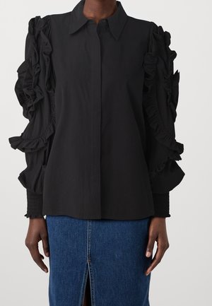 Sort bluse med lange ærmer, flæser på ærmerne, knapper foran og en tekstureret finish. Matchende med en denimnederdel med frontslids.