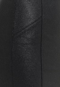 Svarta stretchningsbyxor med en glänsande finish, som har en slät textur och diskreta sömmar längs sidorna.