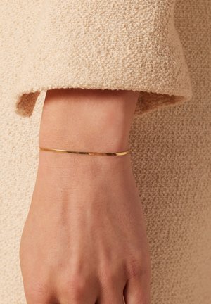 Goldarmband an einem Handgelenk, mit einem eleganten, minimalistischen Design, glatter Oberfläche und subtilen Texturdetails.