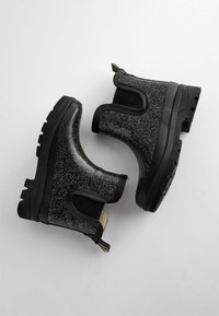 Bottines noires avec une texture pailletée, des panneaux élastiques sur les côtés et une semelle en caoutchouc noire épaisse, dotées d'une languette à l'arrière.