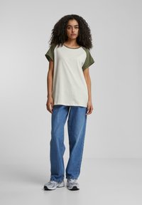 Lyse farget, kortermet t-skjorte med olivengrønne detaljer; kombinert med løse blå jeans og grå treningssko. Jevn stofftekstur.