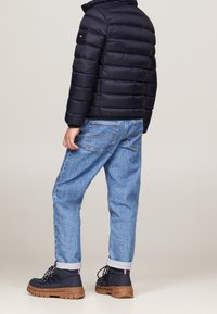 Czarna kurtka puchowa z poziomymi przeszyciami, niebieskie dżinsy oraz granatowe buty turystyczne z grubą brązową podeszwą i logo.