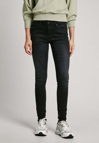 Juodi liesi džinsai, pagaminti iš džinsinio audinio, su klasikinio penkių kišenių dizainu ir subtiliais siuvinėjimo akcentais. Dėvimi su pilkais sportiniais batais.