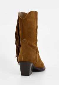 Brązowy zamszowy kowbojski but do połowy łydki z piętą na klocku i frędzlami na tylnej stronie.