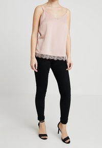 Camisole en satin rose pâle avec une bordure en dentelle à l'ourlet, associé à un jean skinny noir et des escarpins noirs à bout ouvert. Bretelles spaghetti ajustables.