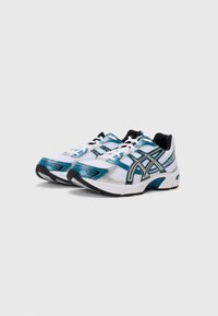 Des chaussures de sport blanches avec des accents turquoises et noirs. Elles présentent des panneaux en maille, un bout arrondi, un col rembourré et des lacets contrastants.