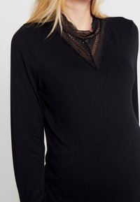 Svart långärmad topp med spetsdetalj vid V-ringningen, mjukt tyg och en figurnära siluett, lämplig för avslappnad eller halvformell klädsel.