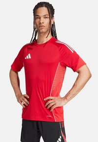 T-shirt de sport rouge avec col rond, manches courtes et bandes blanches. Fabriqué en tissu qui évacue l'humidité avec des panneaux latéraux texturés.
