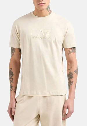 Camiseta de manga corta beige hecha de algodón suave, con un logo en relieve de EA7 Emporio Armani en el frente. Cuello redondo y corte relajado.