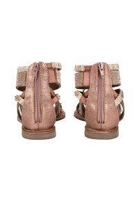 Para różowych sandałów o fakturowanej powierzchni z tylnymi zamkami, z paskami na kostkę ozdobionymi cyrkoniami i płaskimi brązowymi podeszwami, pokazana z tyłu.