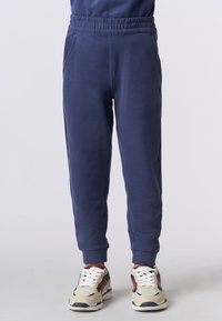 Pantaloni della tuta blu navy con vita elastica, tasche laterali e polsini a costine. Tessuto morbido con una trama semplice. Abbinati a sneakers beige.