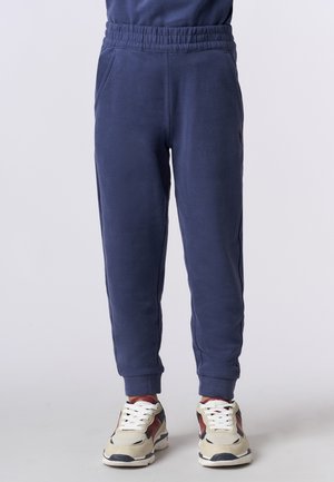 Pantaloni della tuta blu navy con vita elastica, tasche laterali e polsini a costine. Tessuto morbido con una trama semplice. Abbinati a sneakers beige.