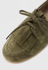 Mocassino in camoscio verde oliva con dettagli sfrangiati, punta tonda e chiusura con lacci. Presenta occhielli metallici e una finitura testurizzata.