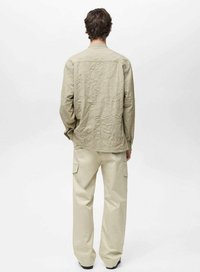 Camicia crinkled beige chiaro con maniche lunghe, cucitura alla yoke posteriore, abbinata a pantaloni cargo beige larghi con tasche laterali.
