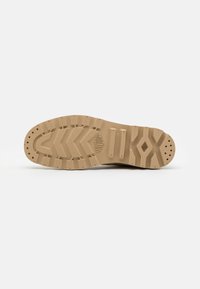 Suola di sneaker beige con superficie in gomma testurizzata, motivo a zigzag e fori di drenaggio per una migliore aderenza e trazione.