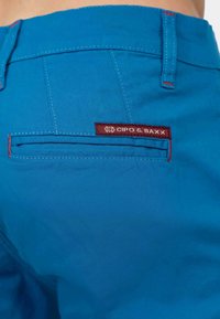Blauwe stoffen shorts met een achterzak met rode stiksels en een bordeauxrood label met het merk "Cipo & Baxx." Soepele textuur met platte naden.