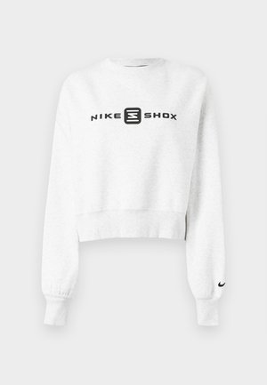 Witte cropped sweatshirt met lange mouwen, voorzien van een zwart 'NIKE SHOX' logo op de voorkant en een kleine zwarte Nike swoosh op de manchet.