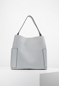 Sac cabas en cuir gris avec une texture douce et lisse, comprenant deux poches latérales, un haut incurvé et une seule bandoulière.