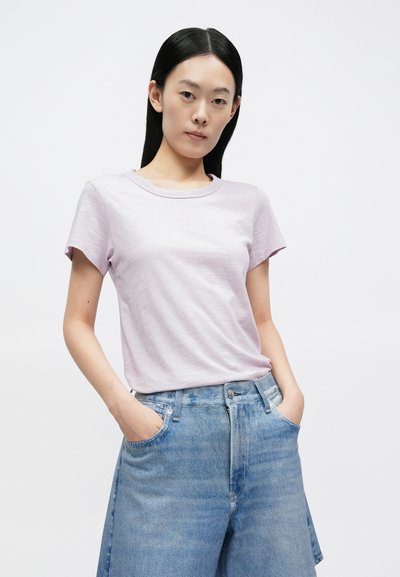 T-shirt de manga curta em lilás claro com gola redonda, combinada com calções de ganga azuis de cintura alta com bolsos frontais.