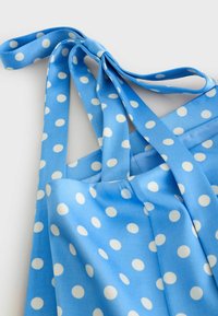 Sac fourre-tout en tissu bleu à pois blancs, avec des anses plates nouées, sur un fond clair.