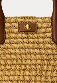 Vævet stråhåndtaske i naturlig tanfarve med brune læderhåndtag og en guldfarvet logo-plade med initialerne "RLL" på en brun baggrund.