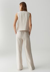 Top beige senza maniche abbinato a pantaloni larghi e chiari beige. Entrambi i capi presentano una texture morbida e un design minimalista.