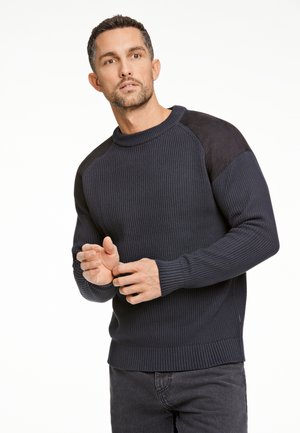 Donkerblauwe geribde trui met zwarte suède schouderaccenten, ronde hals, lange mouwen en aansluitende manchetten. Casual ontwerp met een textuurafwerking.
