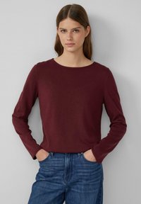 Burgunderfarbener Longsleeve aus weichem Stoff mit rundem Ausschnitt. Kombiniert mit blauen Jeans, die einen lässigen Schnitt und ein einfaches Design aufweisen.