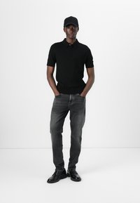 Svart polo skjorte, grå jeans og svarte sko. Poloen har krage og korte ermer. Jeansene har slim fit med diskrete detaljer.