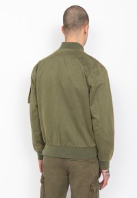 Chaqueta bomber verde oliva con cuello y puños acanalados, con una textura suave y dobladillo elástico, diseñada para un ajuste relajado.