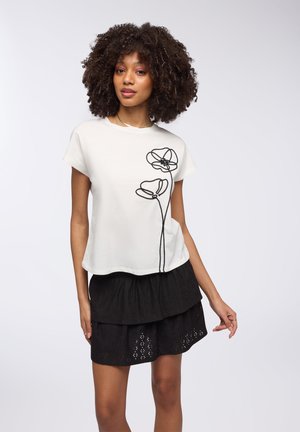 T-shirt bianco a maniche corte con ricami floreali neri sul davanti. Indossato con una gonna nera a volant. Tessuto morbido.