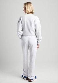 Felpa grigia con spalle scese abbinata a pantaloni della tuta grigi coordinati. Tessuto in cotone morbido; vestibilità comoda e vita elastica.