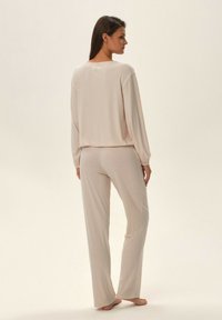 Jasnoróżowy zestaw odzieży do noszenia w domu z prążkowaną fakturą. Bluzka ma długie rękawy i okrągły dekolt, a spodnie są prostego kroju.