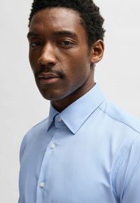 Camicia button-upazzurra con una texture liscia, colletto standard e un motivo sottile; presenta bottoni bianchi e una vestibilità sartoriale.