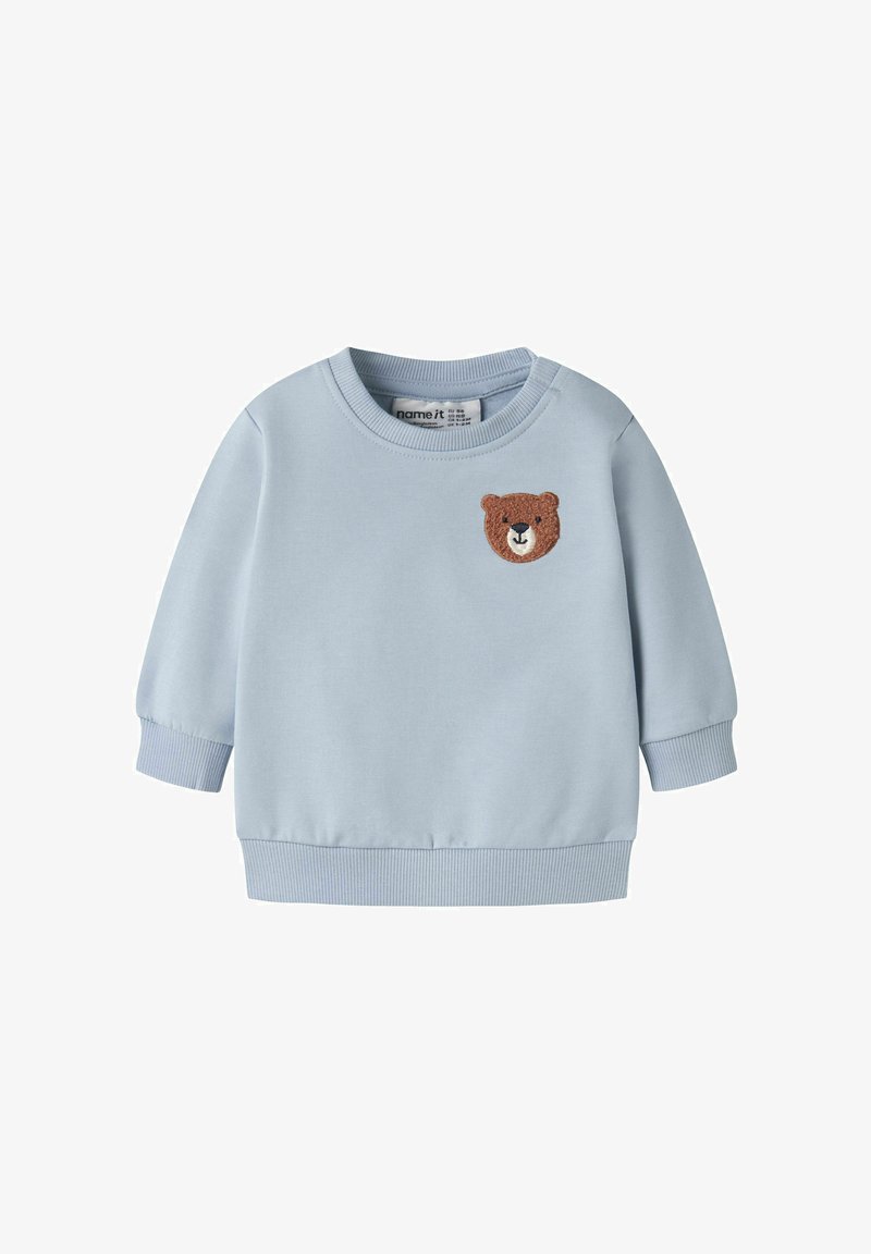 Sweatshirt pour tout-petit bleu clair avec poignets et ourlet côtelés, comportant un petit patch visage d'ours en peluche marron sur la poitrine.