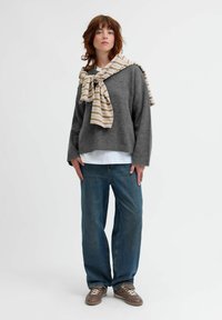 Grå stickad tröja med vid halsringning, som bärs med en vit skjorta. Ljusblå raka jeans och bruna snörskor. Randig scarf hängande.