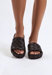 Sandali slide neri intrecciati con finitura in pelle testurizzata, caratterizzati da fasce larghe e design open toe, adatti per un uso casual.